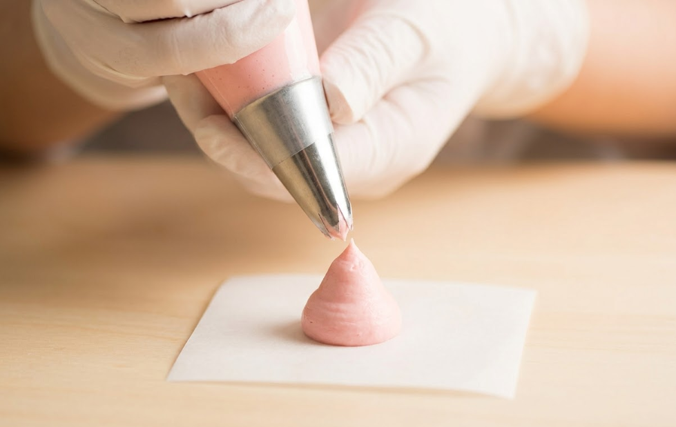 A step-by-step visual of piping a buttercream rose on parchment paper using a piping bag and petal tip, hands in action, close-up shot, soft lighting, detailed texture of frosting, instructional style photography